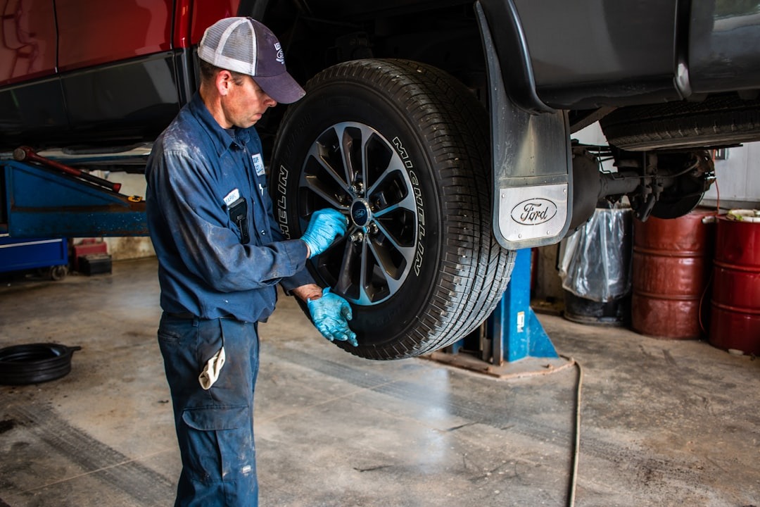 Mechanic in blue uniform fixing truck wheel on lift.